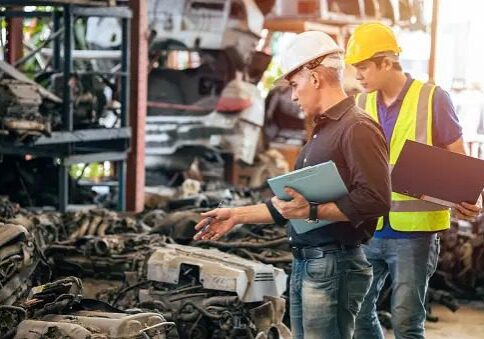 Two men in hard hats looking at a pile of metal.