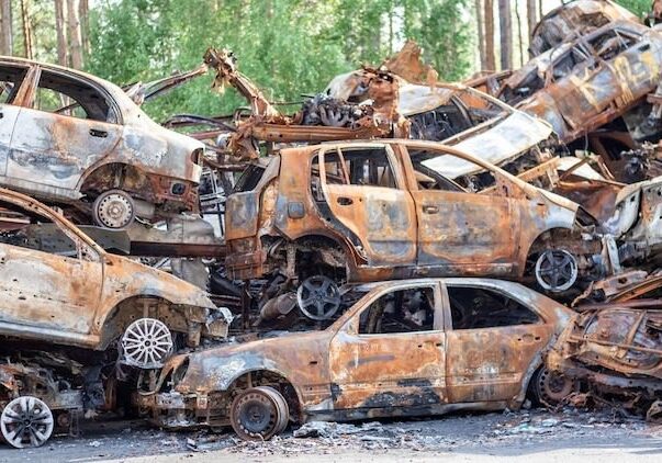 A pile of burnt out cars on the side of the road.